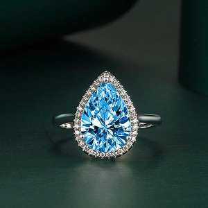 Macro shot of pear-cut blue zircon ring with halo setting on dark green surface