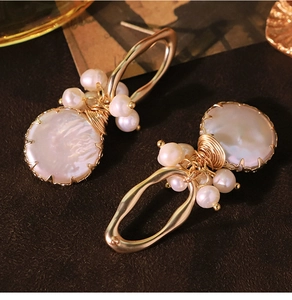 Macro detail of baroque pearl earrings with golden wire wrap on dark matte surface