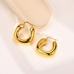 Polished gold hollow U-shaped hoop earrings displayed on a minimalist ceramic tray