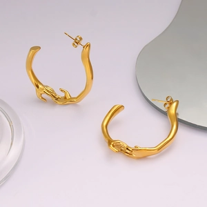 Détail des boucles d'oreilles créoles dorées en forme de mains tenant sur miroir