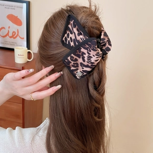 Leopard print bow hair claw clip displayed on hair in a cozy warm-toned setting