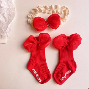 Detailed view of red knitted baby socks and lace headband set with large organza bows
