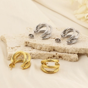 Detail showing gold and silver C-shaped twisted hoop earrings on a beige stone base