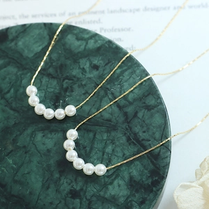 Gold-plated titanium steel necklace with white imitation pearls on a green marble base