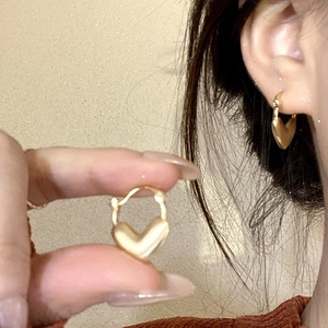 Detailed view of matte gold heart earrings showing 3D shape and model ear styling
