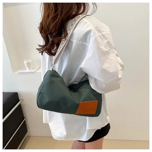 Close-up of green nylon crossbody bag with patterned strap on a white shirt model
