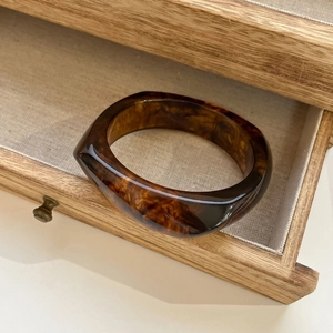 Macro view of wide resin bangle featuring amber marble texture inside a wooden drawer