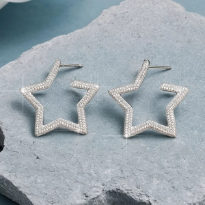 Macro view of silver star earrings with pavé crystals on a natural grey rock background