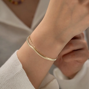 Detail showing a layered gold flat snake chain and delicate bead bracelet on wrist