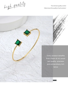 Detailed macro view of an open gold bangle featuring two emerald green square zircon stones