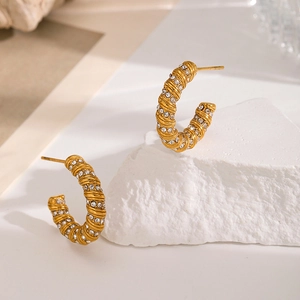 Macro shot of gold-plated C-shaped earrings with twisted texture and crystal inlay