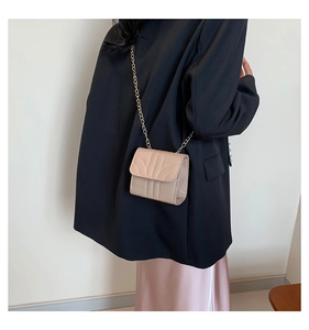 Detail of elegant beige mini square bag with golden chain strap on a model outfit