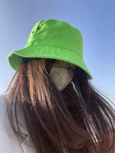 Low angle view of a green cotton bucket hat worn against a clear blue sky background