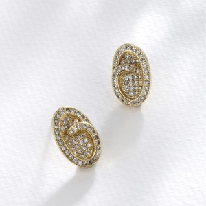 Elegant gold oval stud earrings set with pavé-set clear crystals on textured background