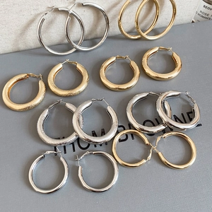 Detail of polished and frosted gold and silver hoop earrings on a textured board