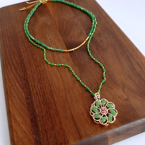 Detail of 18k gold plated glass bead necklace with flower pendant on walnut tray