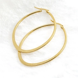 Minimalist high-polish golden oval hoop earrings on soft white plush fabric background