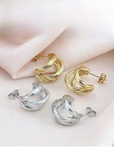 Detail of twisted C-shape hoop earrings in gold and silver finish on silk fabric