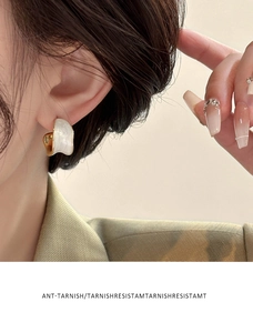 Close-up of 18K gold plated C-shaped earrings with white pearlescent enamel inlay