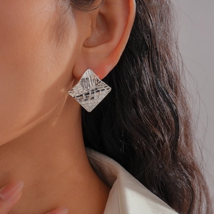 Silver rhombic geometric earrings with micro-checkered texture worn by a female model