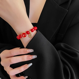 Détail macro du bracelet en perles rouges avec pendentif doré sur une manche