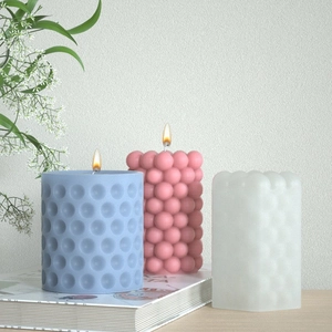 Three textured bubble and dotted cylindrical pillar candles in pastel colors on books