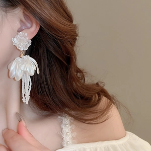 Detail of white flower tassel earrings worn by a model in a minimalist style
