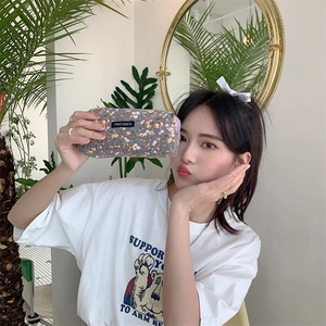 Model holding a dark purple floral corduroy pouch with zipper and brand label