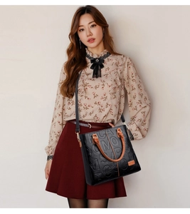 Detailed view of black leather handbag with embossed letters and brown handle strap