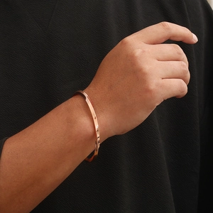 Macro detail of rose gold twisted geometric open bangle with polished metallic finish