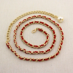 Detail of gold metal chain woven with red leather featuring a large white pearl pendant