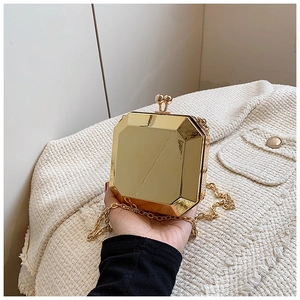 Detail of a golden hexagonal acrylic clutch bag with a sleek metal finish and chain strap