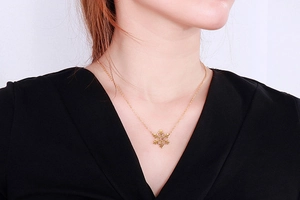 Golden snowflake pendant necklace shown on a model neck with a black V-neck top
