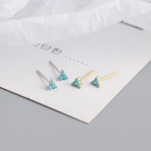 Detail of silver and gold clover earrings with turquoise stones in a minimal flat lay