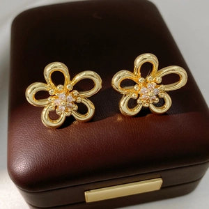 Close-up of golden hollow flower earrings with sparkling cubic zirconia on brown leather