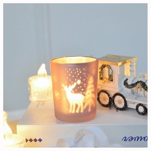 Close-up of frosted pink glass candle holder with glowing reindeer and forest silhouette