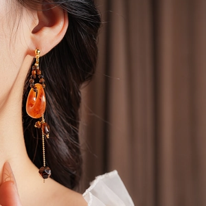 Detail of amber resin drop earring with gold chain and faceted brown beads on model