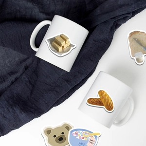 Close-up of cute cartoon food stickers featuring butter and baguette on ceramic mugs