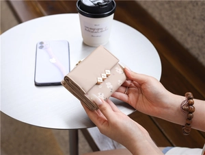 Floral print tri-fold wallet in beige held by a model on a white table setting