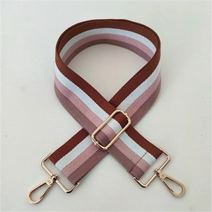 Detail of adjustable striped fabric bag strap with golden metal clasps on white background
