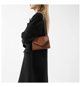 Close-up of brown quilted crossbody bag featuring V-stitch and gold chain strap details