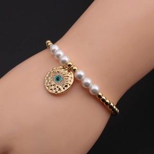 Détail macro du bracelet perlé doré avec pendentif œil maléfique bleu et zircons blancs