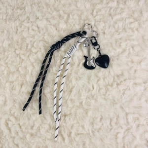 Detail of woven rope keychain with electric guitar and black heart charms on plush fabric