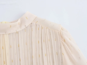 Detailed macro view of beige chiffon dress featuring elegant pleats and metallic sparkles