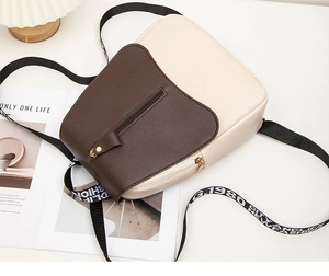 Detail of color-block backpack with dark brown flap and logo strap on white desk