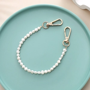 Baroque pearl phone strap with gold lobster clasps displayed on a blue ceramic tray