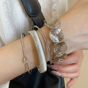 Close-up of four-piece silver metal bracelet set with irregular textures and knot detail