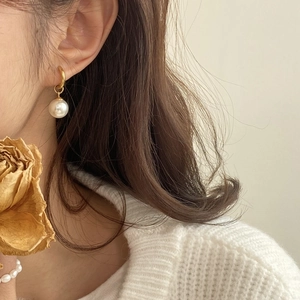 Elegant gold hoop earrings with white pearls on a model wearing a knitted sweater
