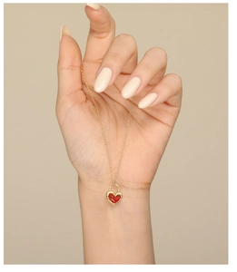 Detailed close-up of a hand holding a red heart agate pendant with gold chain