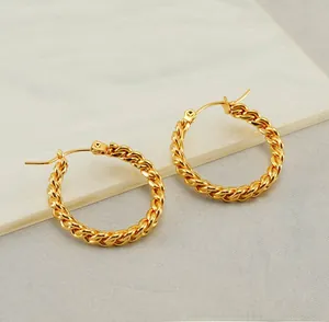Detailed close-up of golden twisted rope hoop earrings on a white marble surface